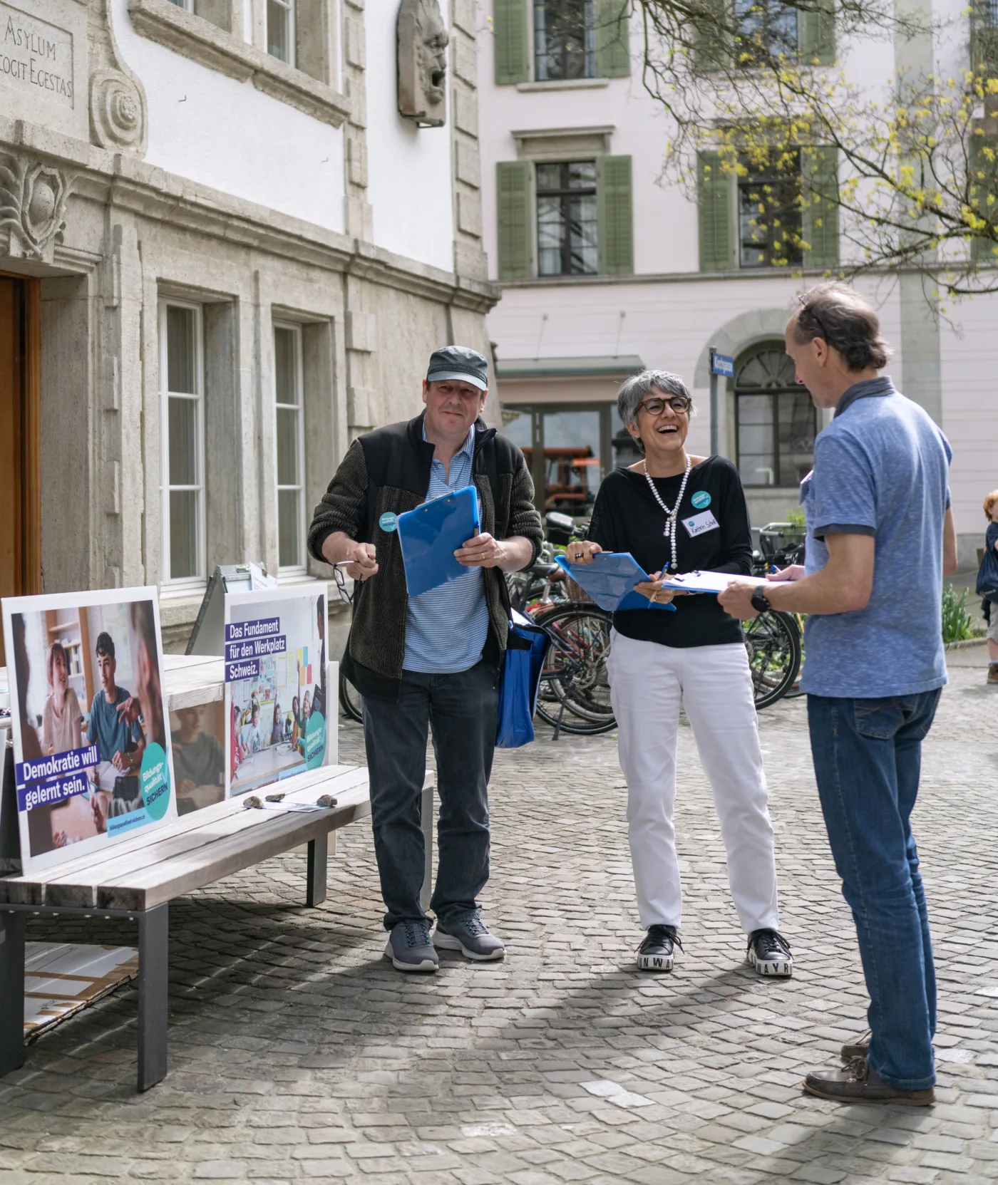 Drei Mitglieder der Geschäftsleitung von Bildung Aargau stehen auf einem Platz in der Stadt Lenzburg und sammeln Unterschriften für die Bildungsinitiative.